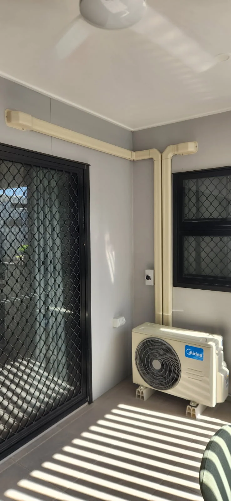 Midea air conditioning outdoor unit on a tiled balcony with conduit running up the wall