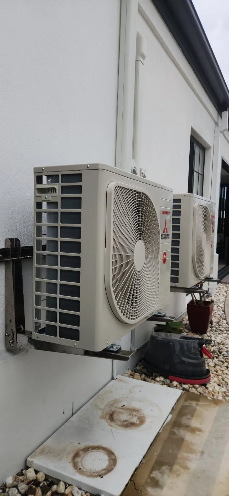 Two Mitsubishi Heavy Industries air conditioning outdoor units mounted on wall brackets on a rendered wall