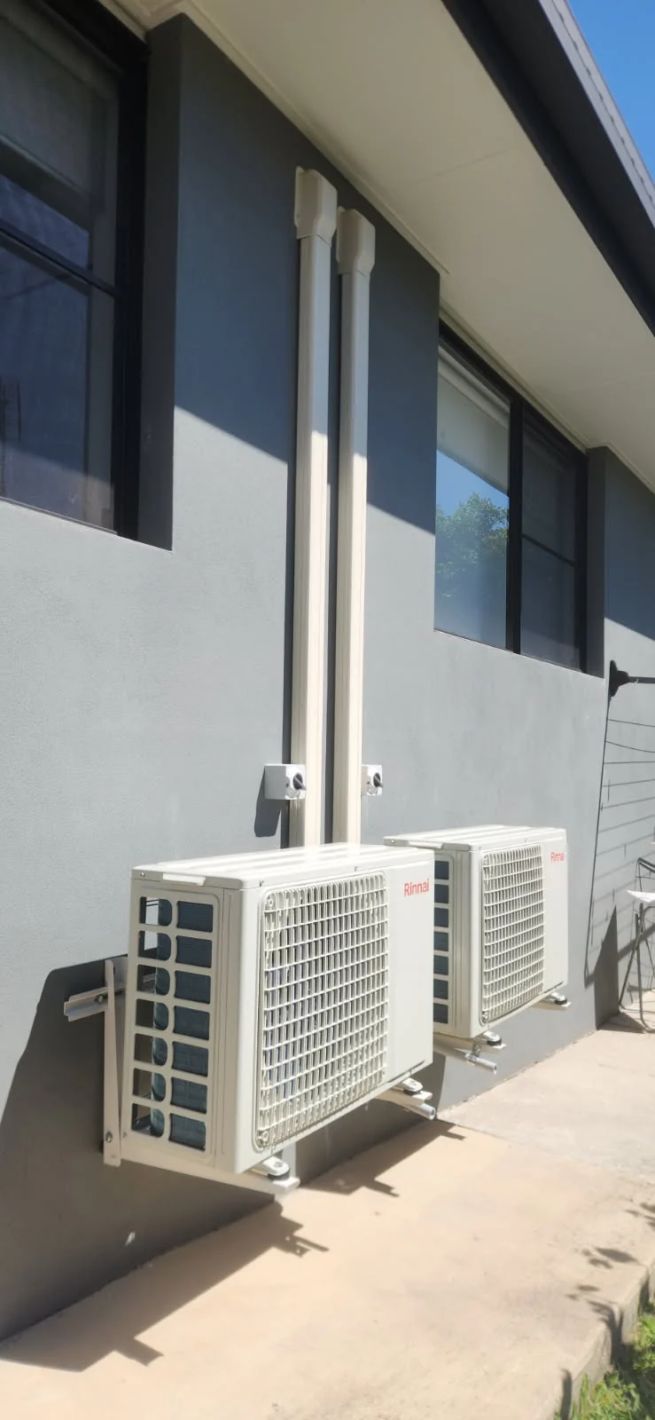 Two Rinnai air conditioning outdoor units on wall brackets against a charcoal rendered wall