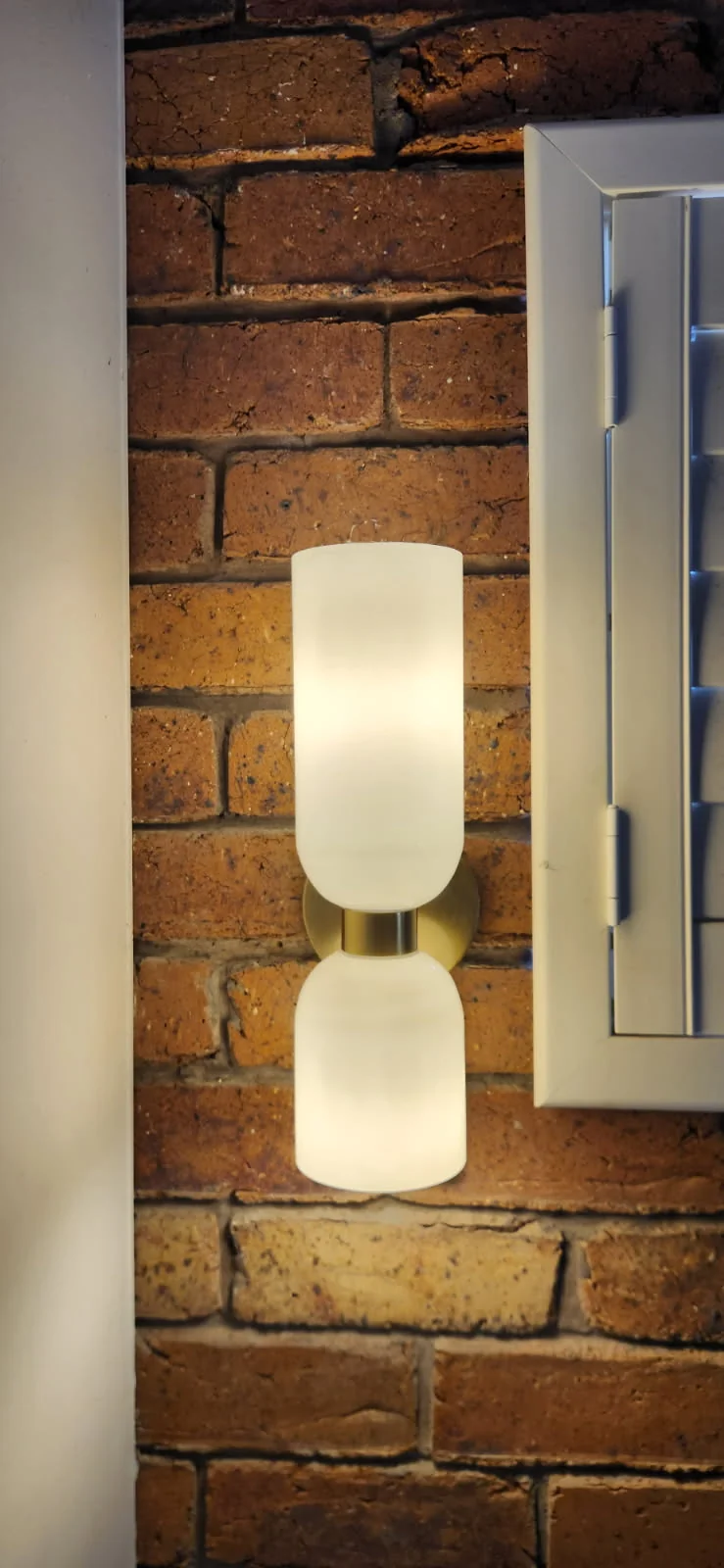 Double frosted-glass wall light with a brass fitting on an exposed red brick wall