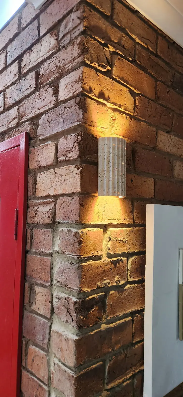 Fluted up/down wall light casting warm light across a red brick corner