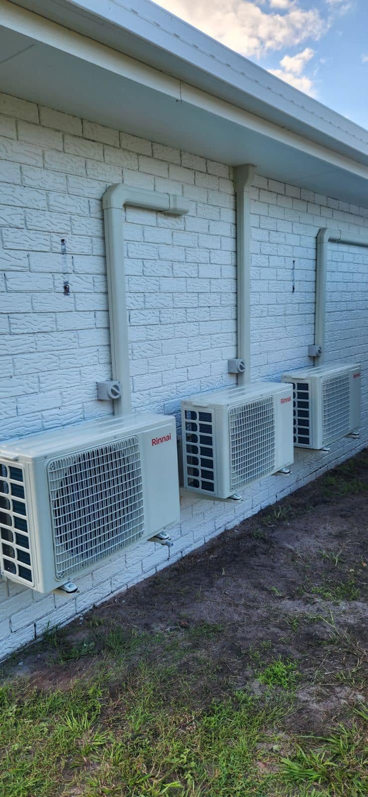 Three Rinnai air conditioning outdoor units lined up along a painted brick wall
