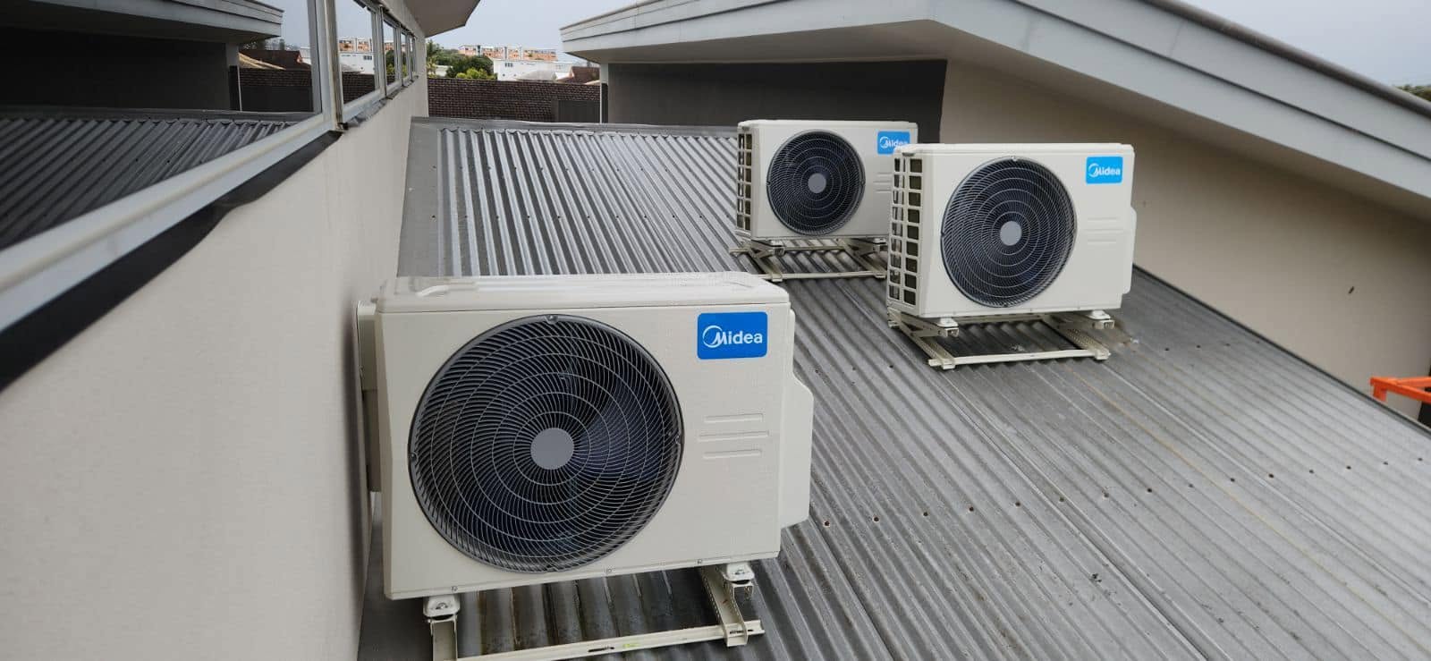 Three Midea air conditioning condensers mounted on a metal roof